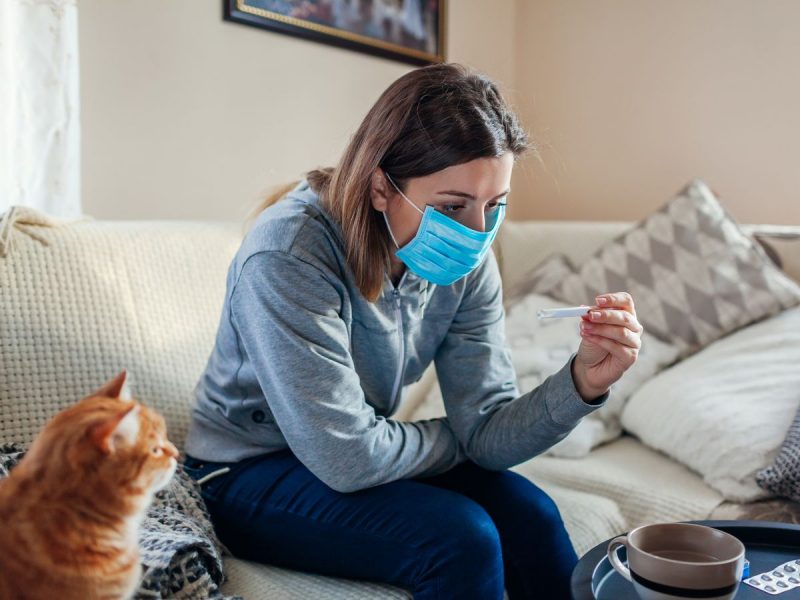 1 Ill woman checking thermometer having fever Girl wearing protective mask while having cold flu at